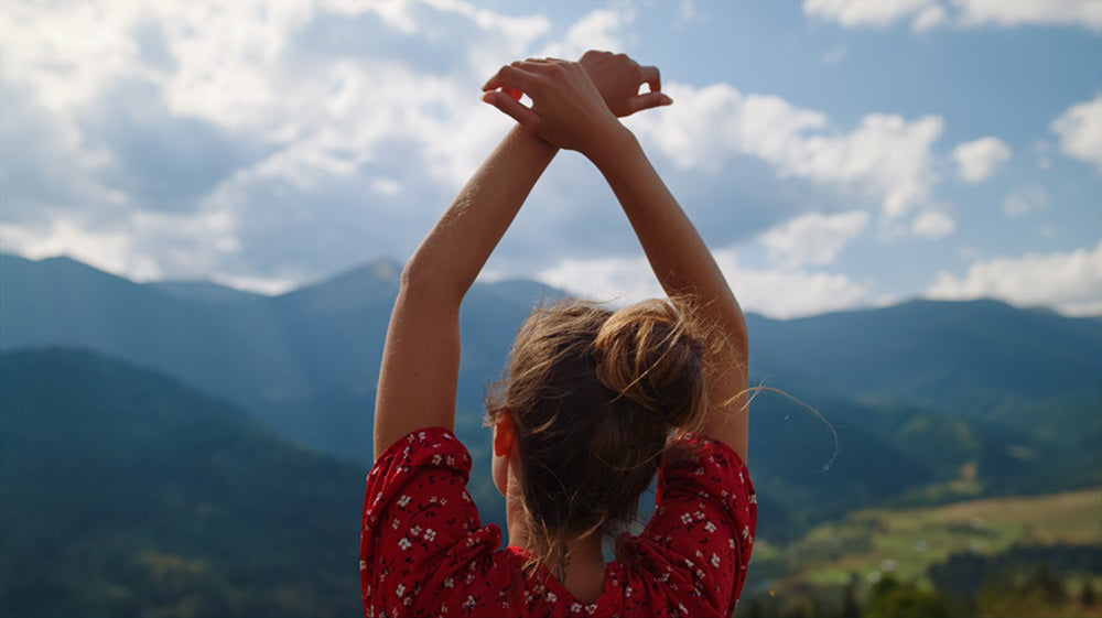 Back of woman with raised hands looking at Eastern mountains & blue sky